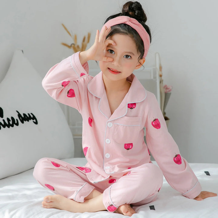 Young girl sitting on bed wearing pink strawberry print pajamas and pink headband