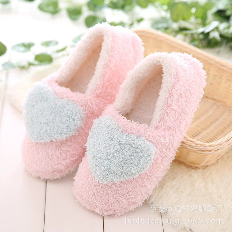 Soft pink fuzzy slippers with large grey heart design, cozy home footwear on white floor