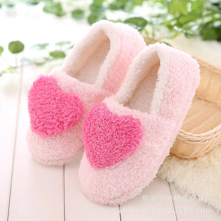 Soft pink fuzzy slippers with large plush pink hearts on top, placed on a white wooden floor