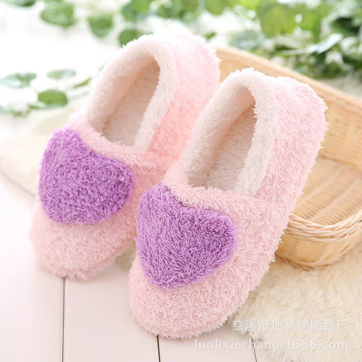 Pink fluffy indoor slippers with large purple heart design, cozy home footwear on white floor