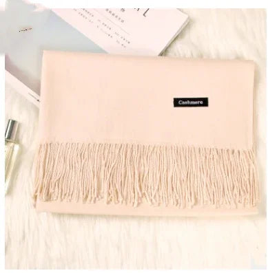 Soft beige cashmere scarf with fringe detail laid on white fur surface