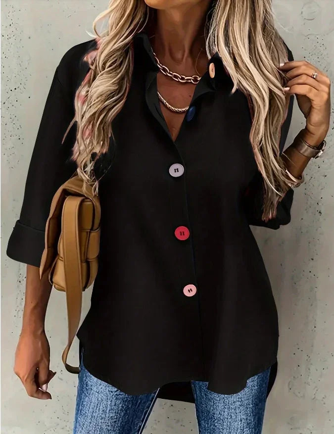 Woman wearing black button-up shirt with colorful buttons, blue jeans, and beige shoulder bag