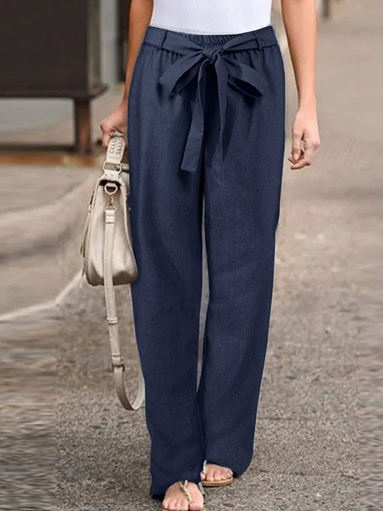 Woman wearing navy blue high-waisted wide-leg pants with a front tie bow, carrying beige handbag, casual outfit