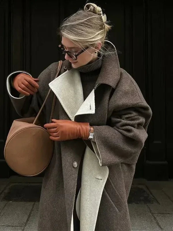 Woman in stylish grey and cream wool coat, tan leather gloves, round brown handbag, and glasses against black background
