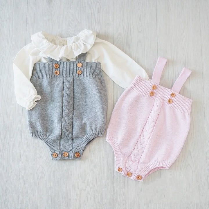 Knitted baby rompers in gray and pink with wooden buttons on light wood floor, one paired with white ruffled blouse