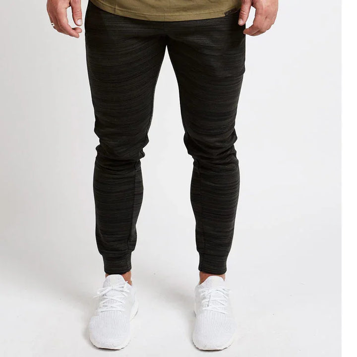 Man wearing black textured jogger pants and white sneakers on plain background