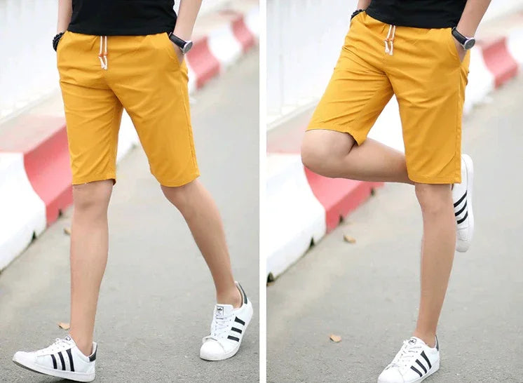 Man wearing mustard yellow drawstring shorts and white sneakers with black stripes on urban street