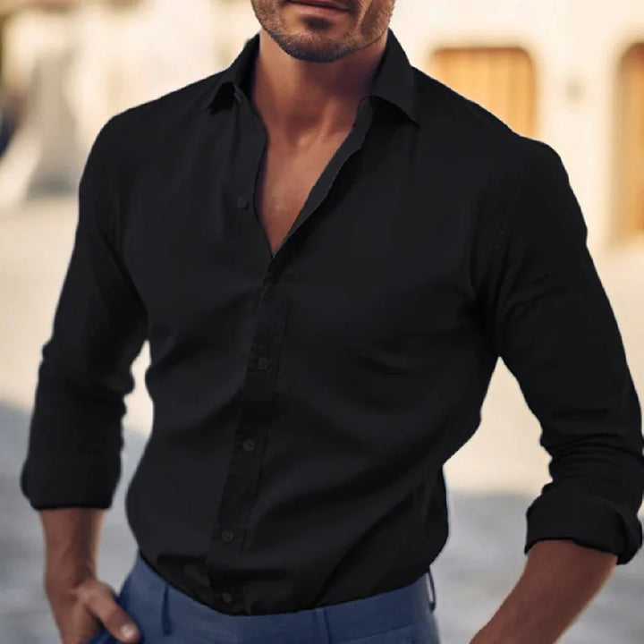 Man wearing fitted black button-down shirt with rolled-up sleeves and blue pants outdoors