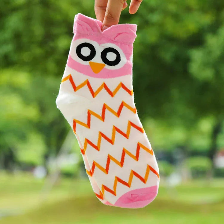 Hand holding a pink and white owl-themed sock with orange zigzag patterns in an outdoor setting