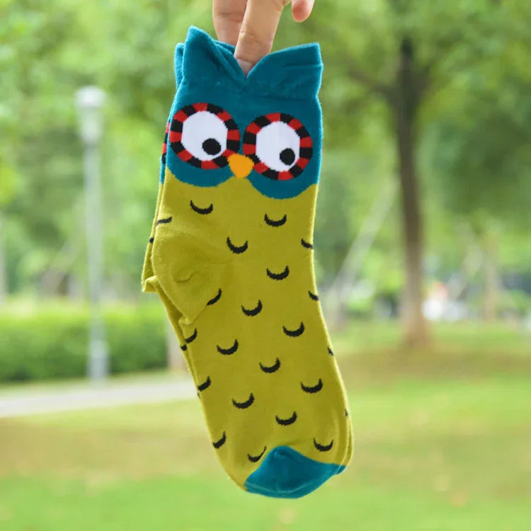 Bright yellow and blue ankle sock with cartoon owl face and patterns, held outdoors with blurred greenery