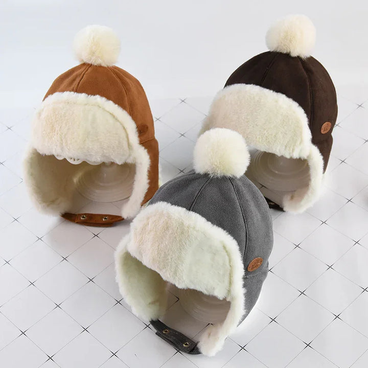 Three plush winter trapper hats in brown, dark brown, and gray with white faux fur lining and pom-poms