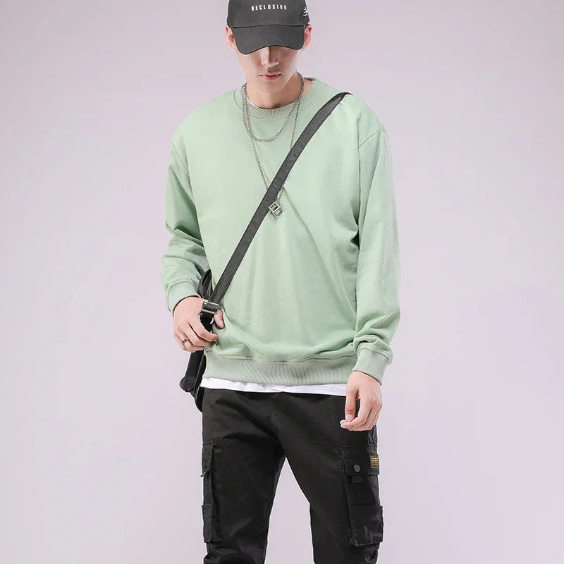 Man wearing sage green sweatshirt, black cargo pants, black cap, silver chains, and black crossbody bag