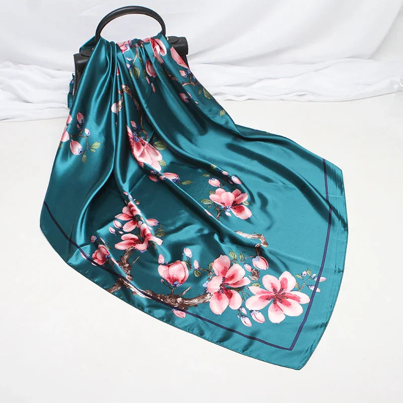 Teal satin scarf with pink cherry blossom design draped over black circular handle on white surface