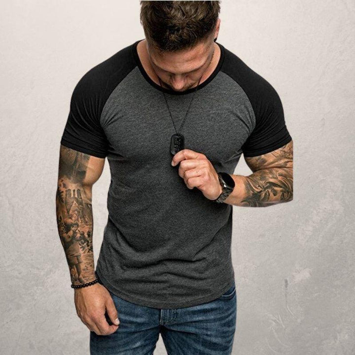 Muscular man with tattoos wearing black and gray raglan t-shirt and blue jeans, looking down