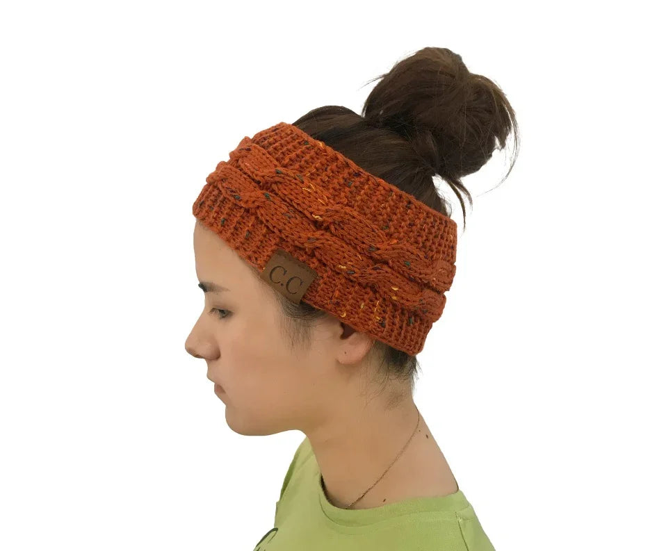 Profile of woman wearing rust orange knit cable headband with brown leather CC tag and messy bun