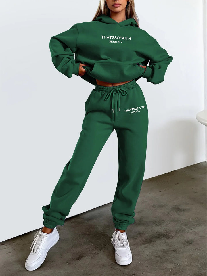 Woman wearing green hoodie and sweatpants set with THATSSOFAITH Series 2 text, white sneakers, casual outfit