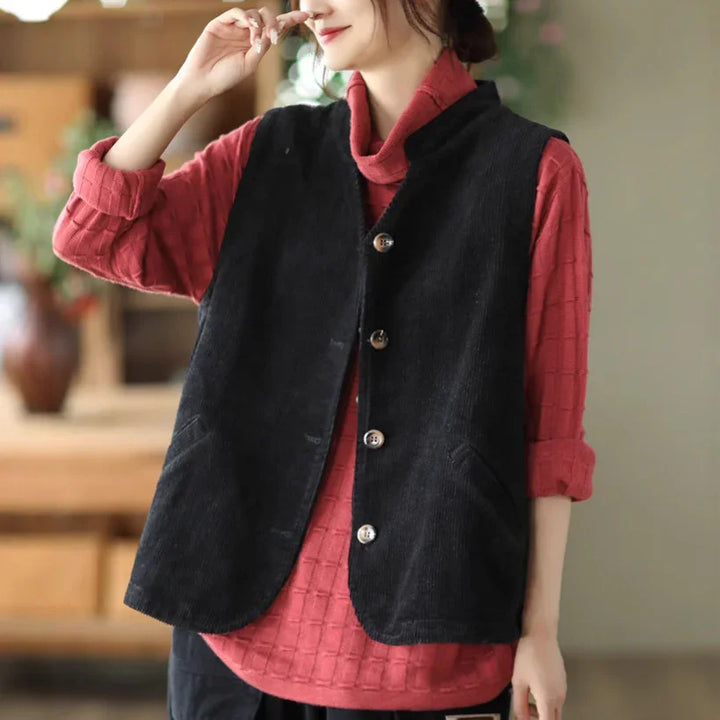 Woman wearing black buttoned vest over textured red long-sleeve top in cozy indoor setting
