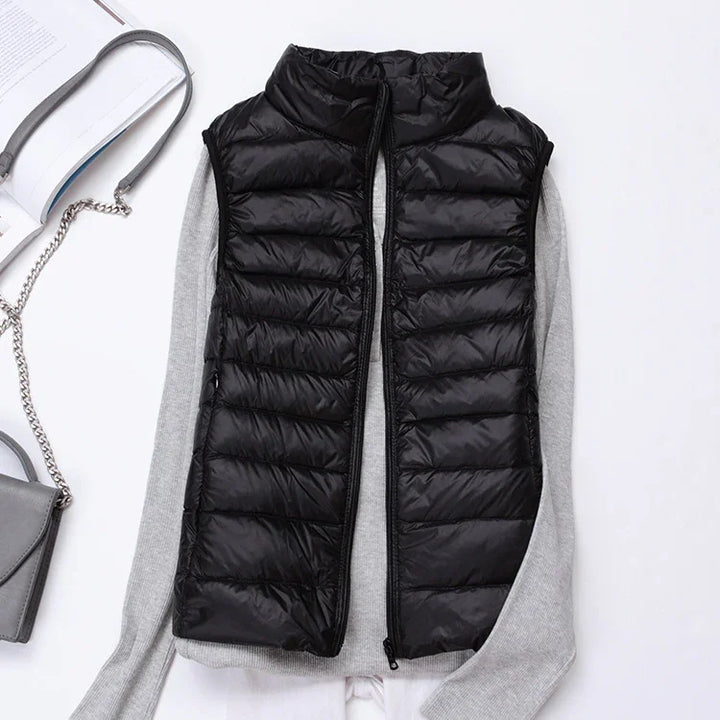 Black quilted sleeveless puffer vest layered over gray long sleeve sweater with open zipper on white background
