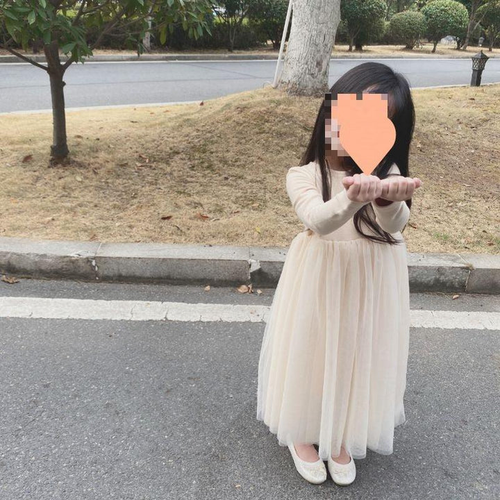Girl in long cream dress and white shoes standing on road with hands extended, trees in background
