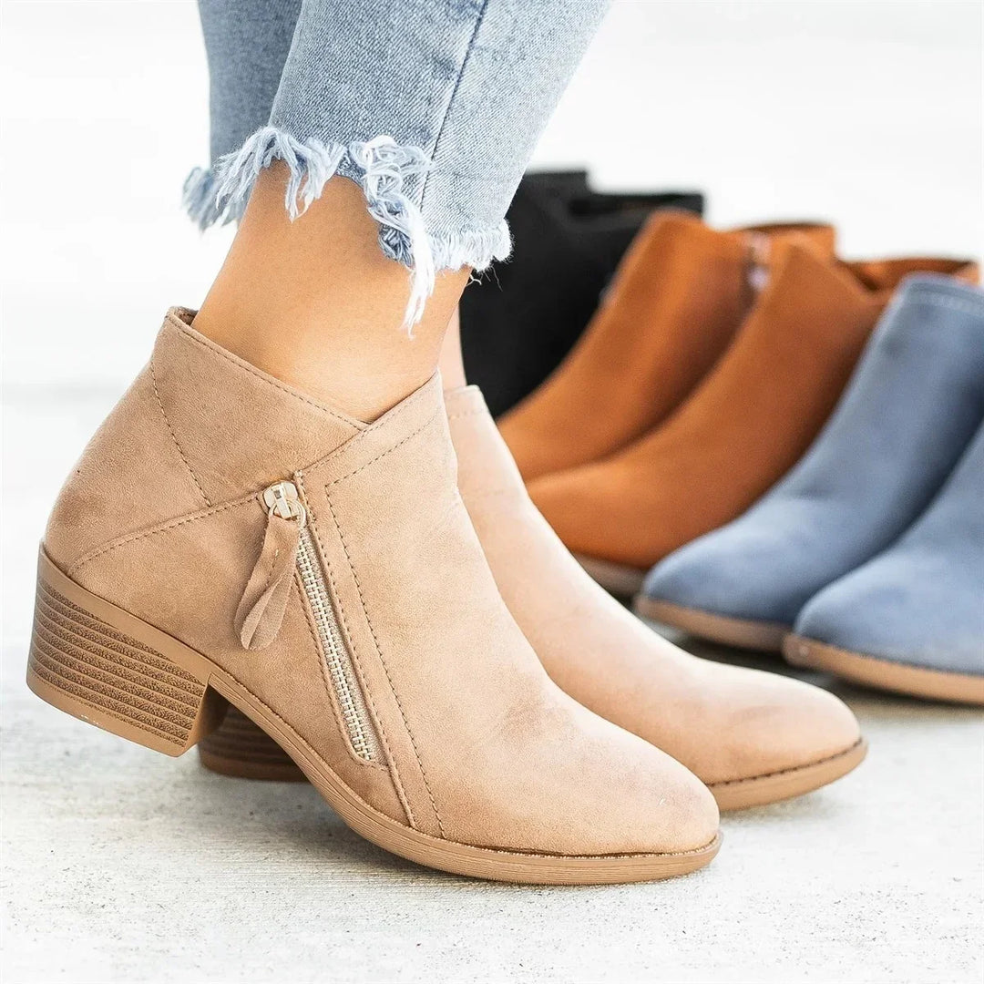 Close-up of beige suede ankle boots with side zipper worn with frayed light blue jeans, other boots in background