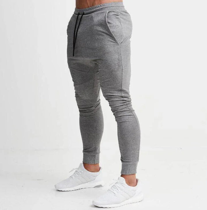 Man wearing slim-fit grey jogger pants with black drawstrings and white athletic sneakers on white background