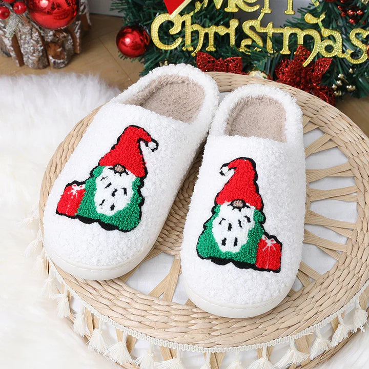 White cozy slippers with embroidered Christmas gnome and red gift on woven mat, festive holiday decor