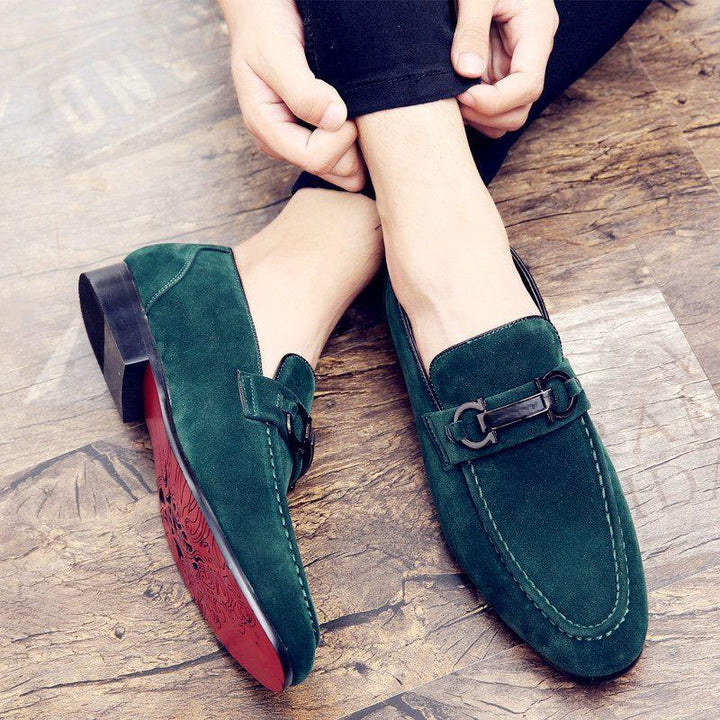 Green suede men's loafers with black decorative buckles on rustic wooden floor