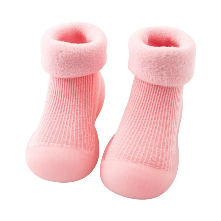 Pair of soft pink baby booties with ribbed fabric and plush cuff, rubber sole for grip