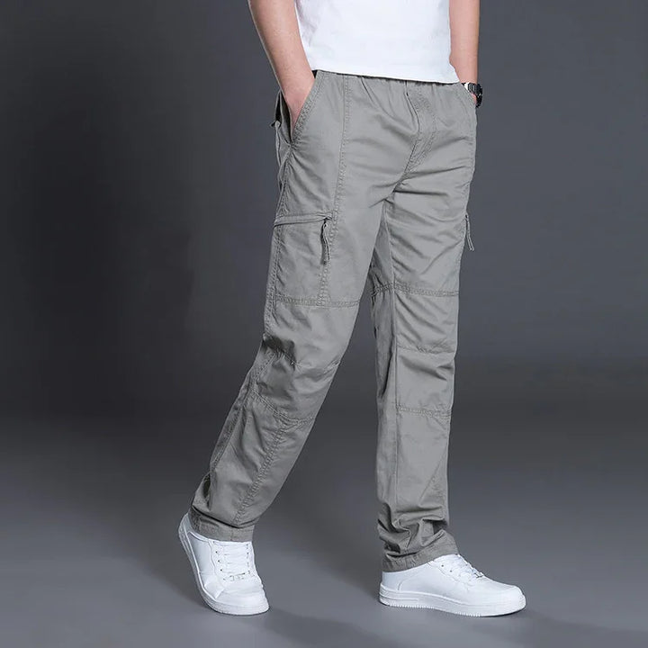 Man wearing gray cargo pants and white sneakers against gray studio background
