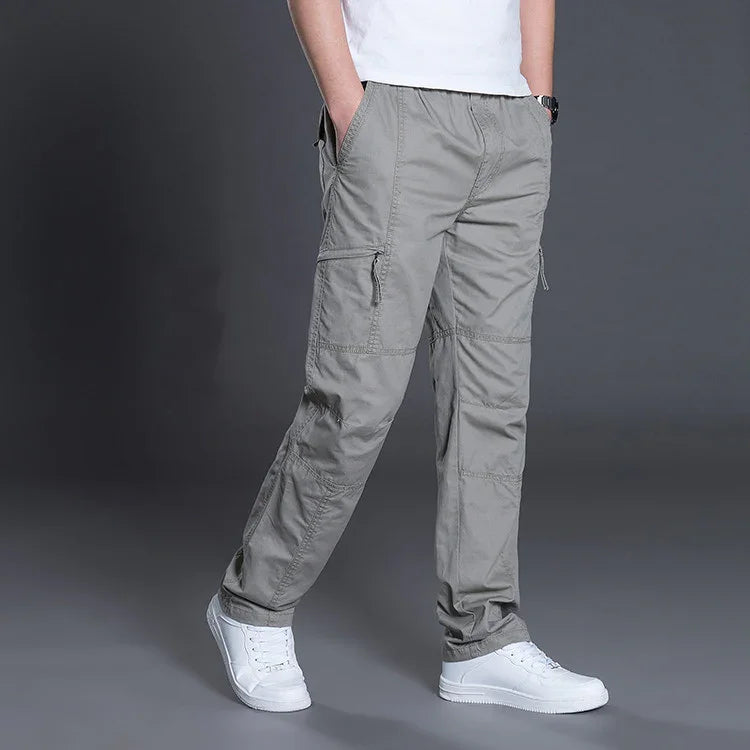 Man wearing gray cargo pants with zippered pockets and white sneakers against gray background