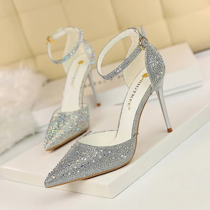 Silver high heel stiletto shoes with ankle strap and rhinestone embellishments on display