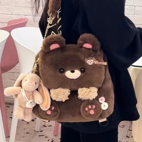 Plush brown bear backpack with pink accents and a beige bunny keychain worn by person indoors