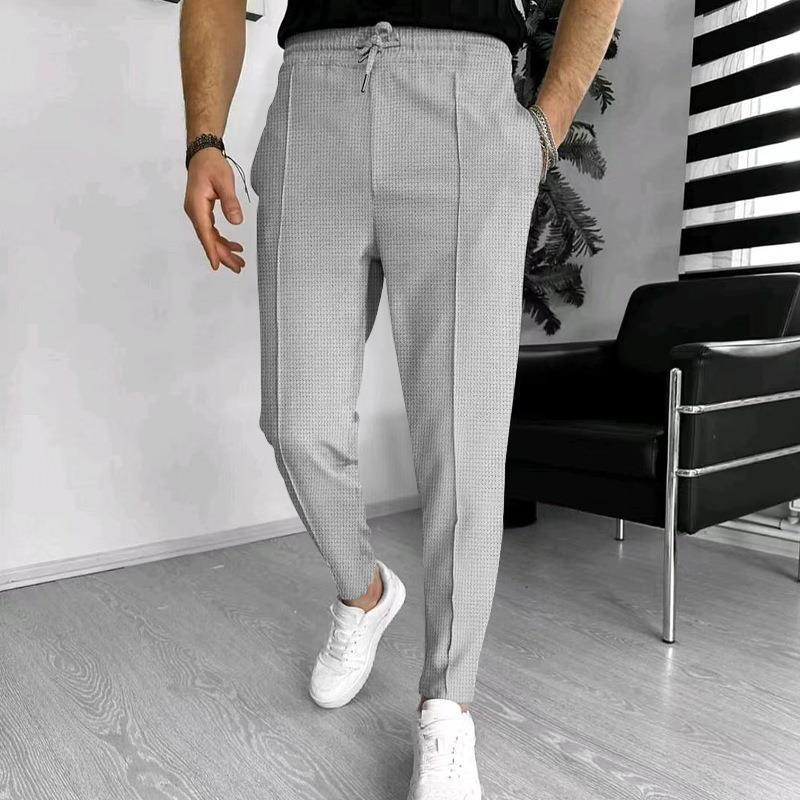 Man wearing light gray textured jogger pants with a drawstring waist and white sneakers in modern room