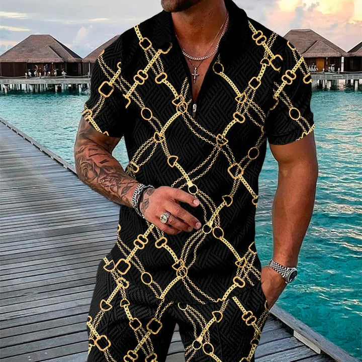 Man wearing black short-sleeve outfit with gold chain and ring pattern, standing on wooden dock by turquoise ocean