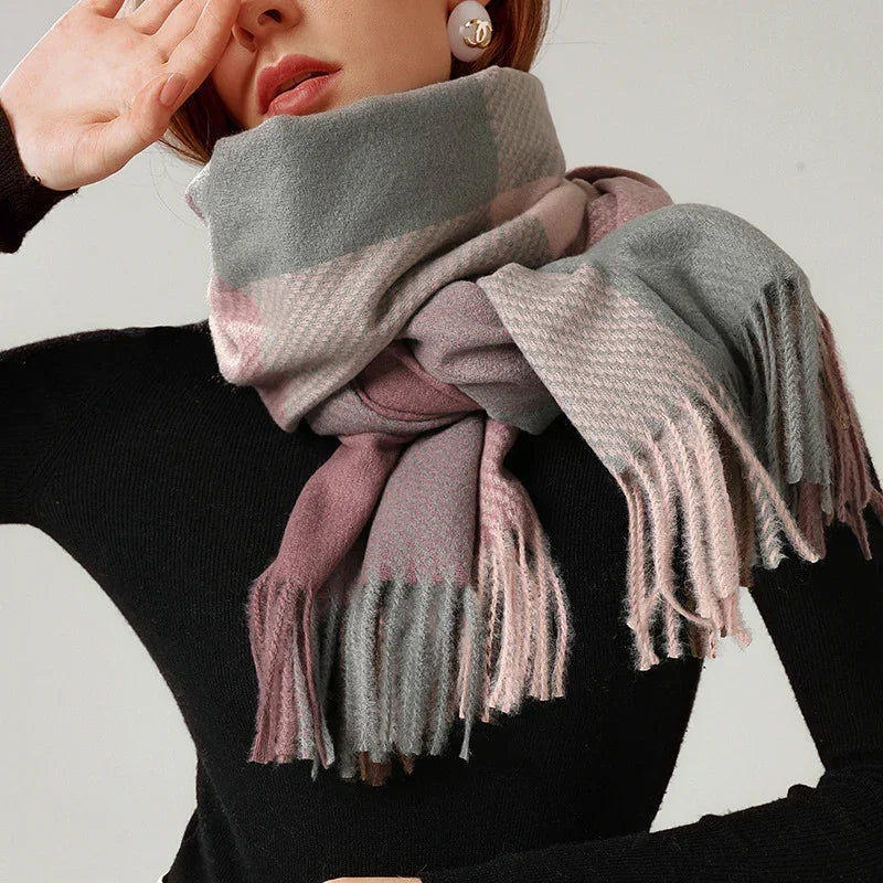 Woman wearing cozy fringed plaid scarf in shades of gray and pink over black sweater