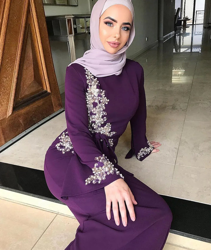 Woman wearing purple embellished dress and light lavender hijab sitting indoors on tiled floor