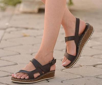 Close-up of woman's feet wearing black wedge sandals with ankle straps on outdoor stone pavement
