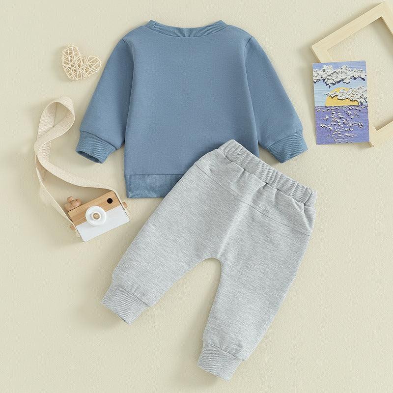 Blue long-sleeve baby sweatshirt and gray sweatpants set on beige background with wooden toy camera