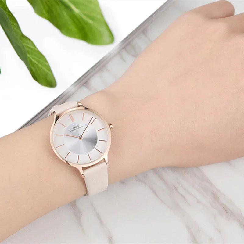 Elegant wristwatch with rose gold case and white leather strap on a wrist, green leaves background