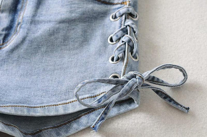 Close-up of light blue denim shorts with side lace-up detail and bow on beige background