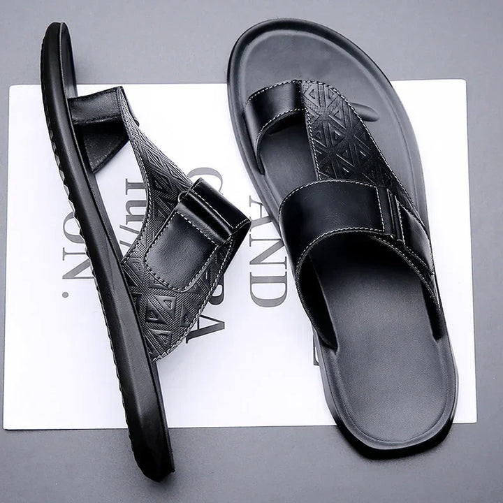 Pair of black men's slip-on sandals with geometric pattern straps on white and gray background