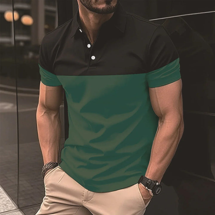 Muscular man wearing black and green short-sleeve polo shirt with beige pants leaning against glass wall