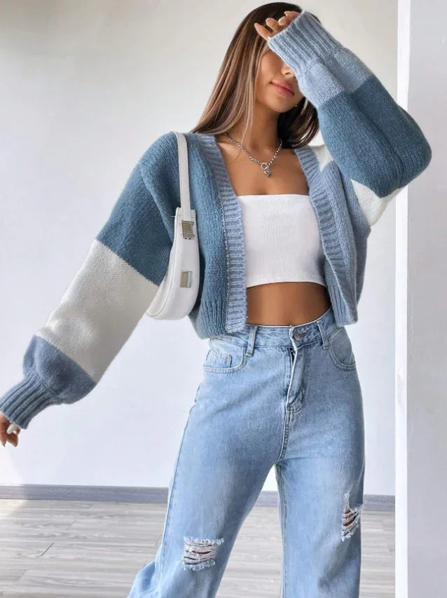 Woman wearing colorblock blue and white knit cardigan, white crop top, distressed high-waist jeans, and white shoulder bag