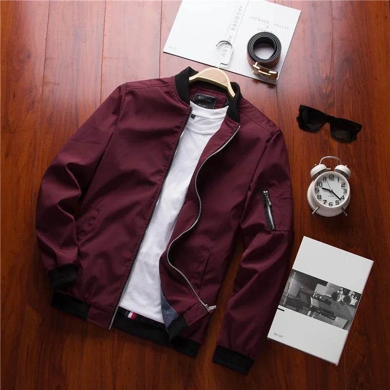 Maroon bomber jacket with black collar and cuffs, white t-shirt, black belt, sunglasses, white alarm clock, and books on wooden floor