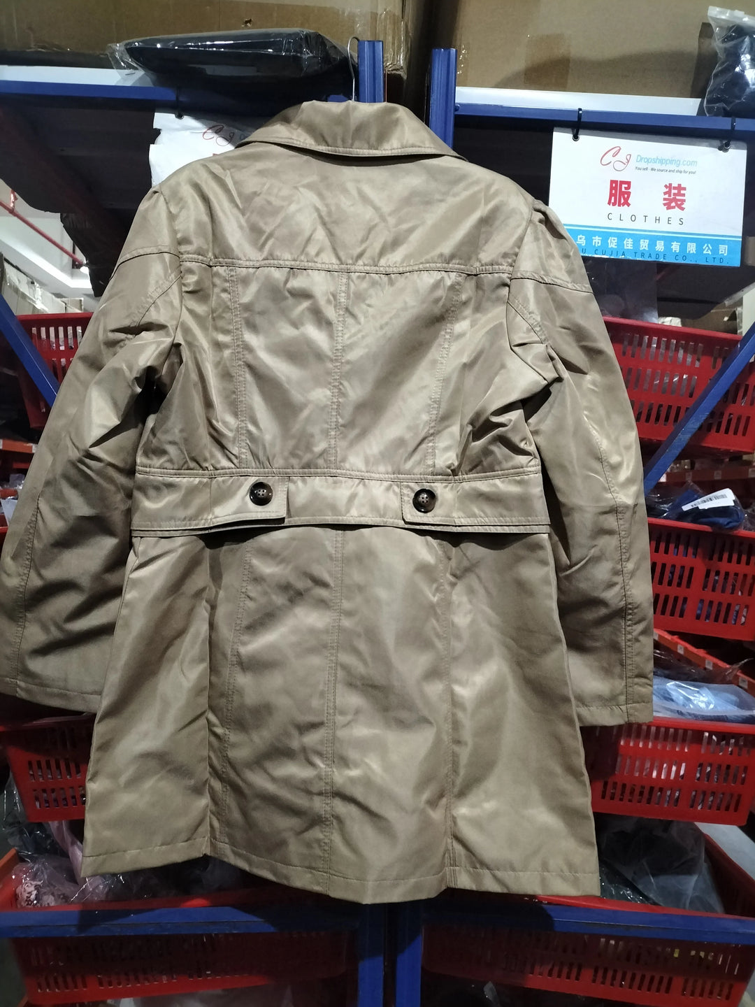 Beige trench coat hanging in a warehouse with red storage bins and clothing sign