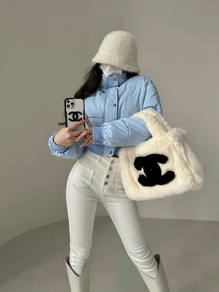 Woman wearing blue puffer jacket, white bucket hat, high-waisted white pants, carrying fluffy white tote bag with black logo
