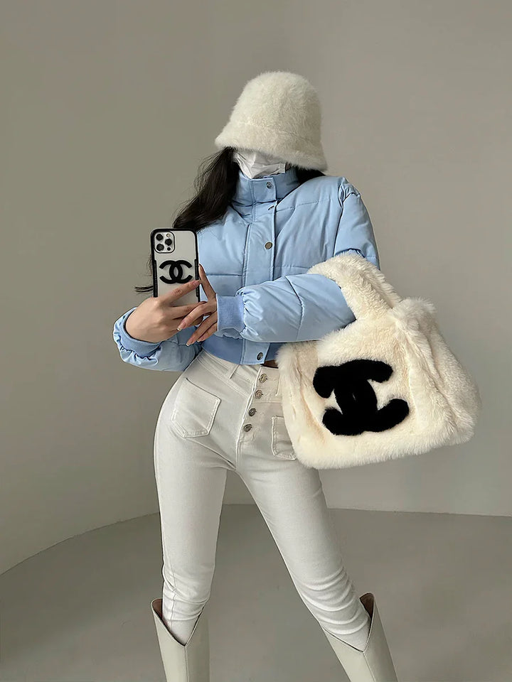 Woman wearing blue puffer jacket, white bucket hat, high-waisted white pants, carrying fluffy white tote bag with black logo