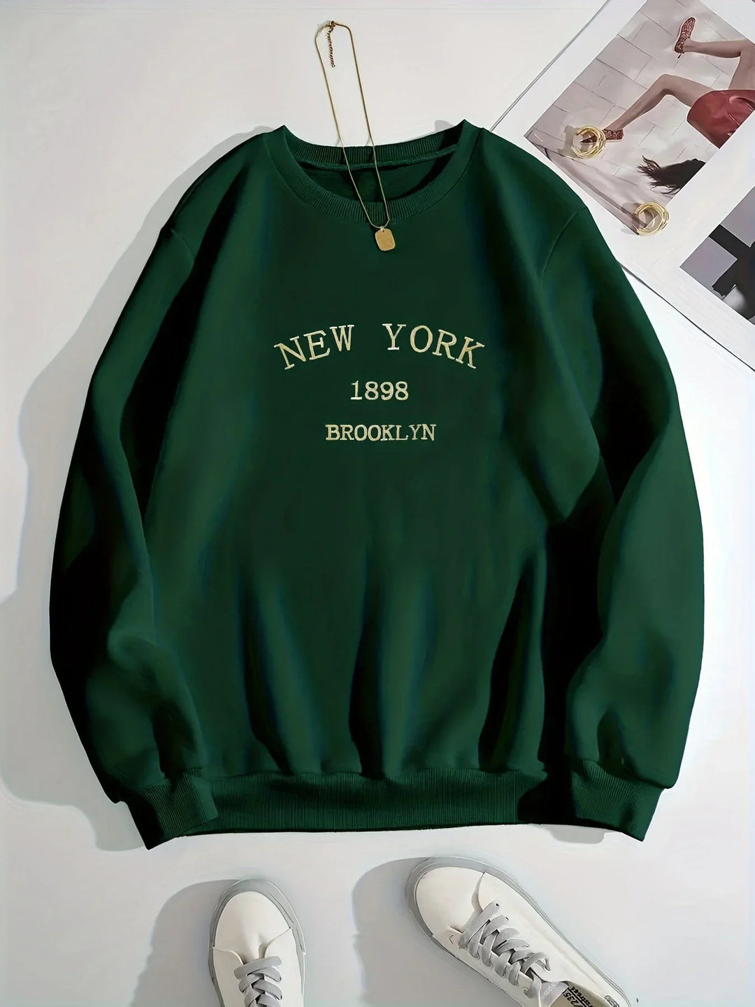 Green New York Brooklyn sweatshirt with 1898 print, white sneakers, and gold necklace flat lay