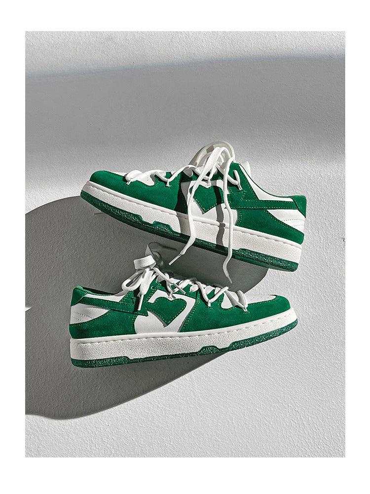 Green and white low-top sneakers with white laces on a light textured surface casting shadows