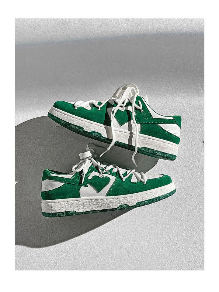 Green and white low-top sneakers with white laces on a light textured surface casting shadows